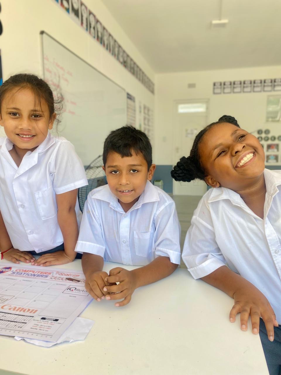 Neatly dressed Olive River Schools learners smiling in a clean classroom